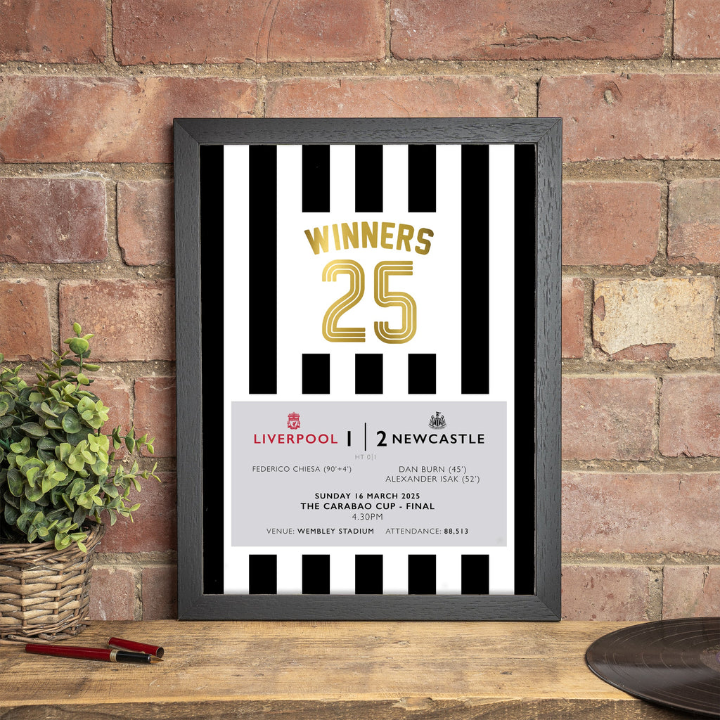 A framed print of the Newcastle United Carabao Cup 2025 Winners, featuring match details and the team's iconic black and white stripes, displayed against a brick wall backdrop.