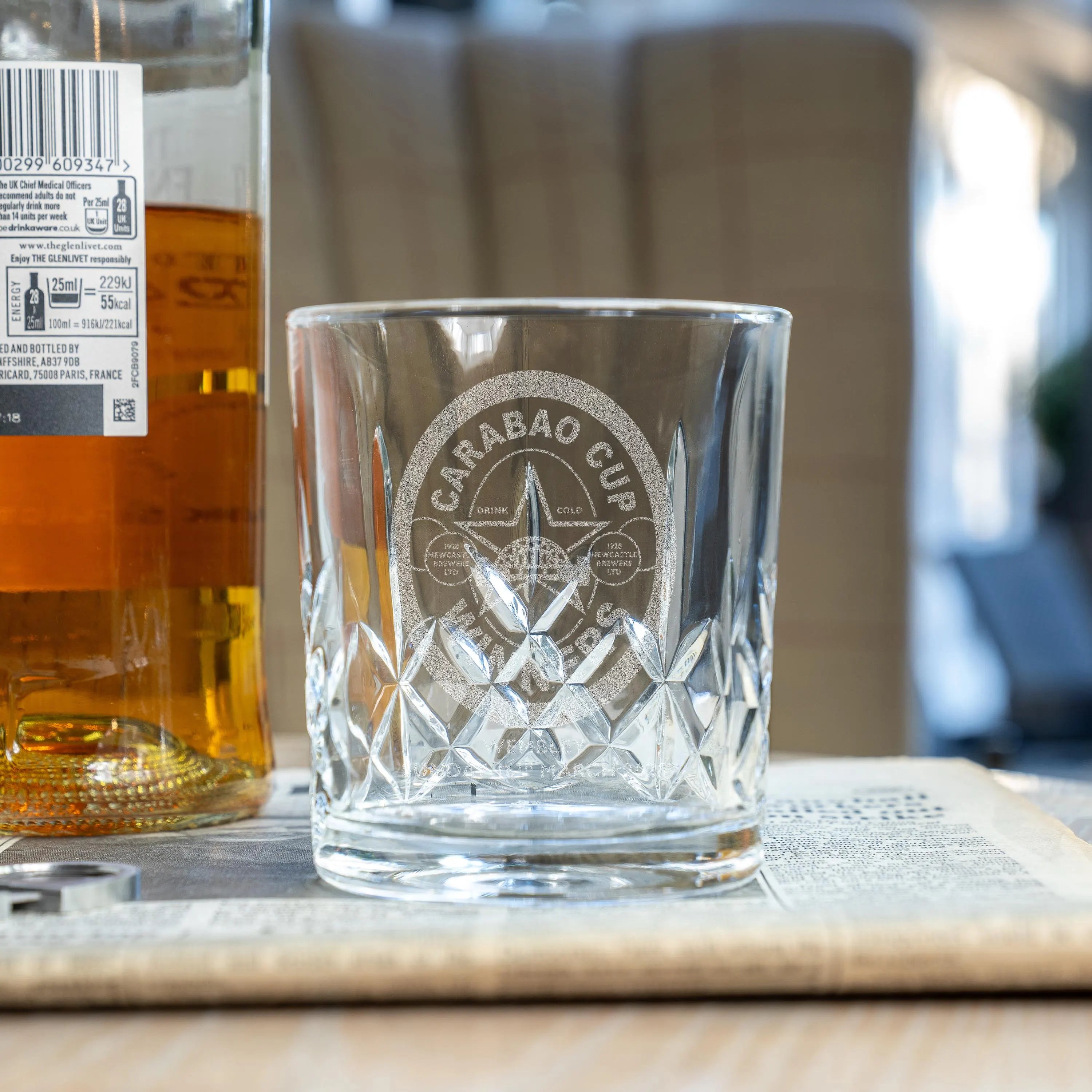 Newcastle United Carabao Cup Winners cut glass whisky tumbler with engraved Wembley 2025 logo, displayed beside whisky bottle.