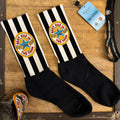 Pair of black-and-white striped socks with “Best Dad in The Toon” badge design laid out on a wooden surface beside a Newcastle Brown Ale bottle and football lanyard.